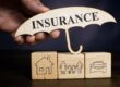 Hand holds umbrella with word insurance and cubes with home, family and car.